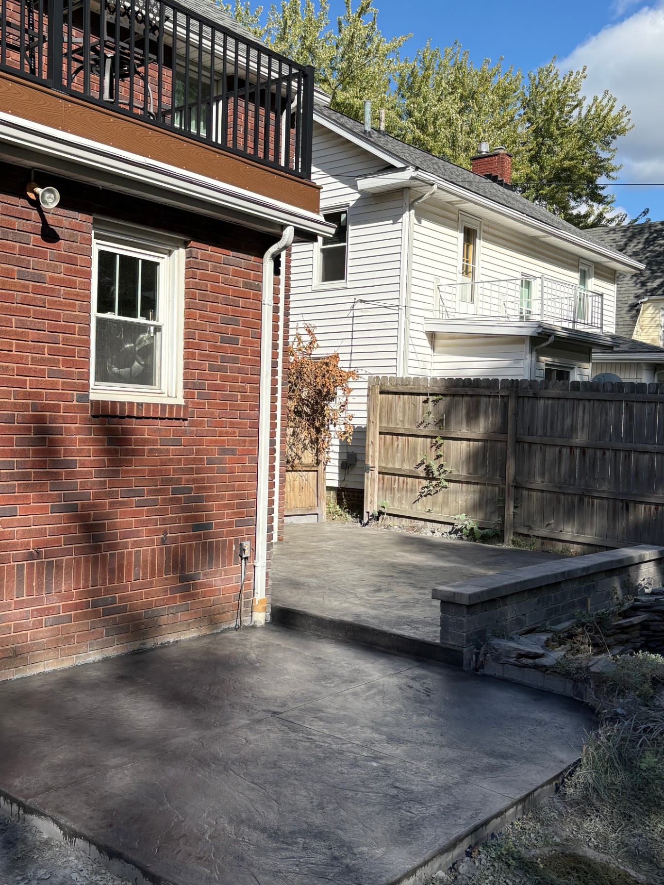 Two-tier stamped concrete patio with stone seat wall behind a brick home in Akron, Ohio