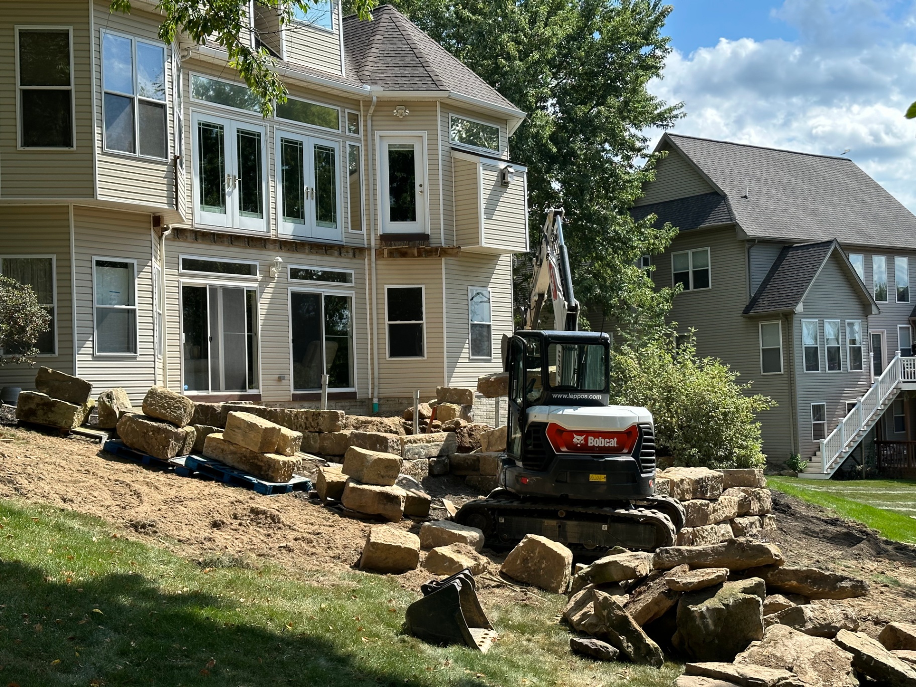Excavator setting large boulders for a retaining wall project at a Medina, Ohio home