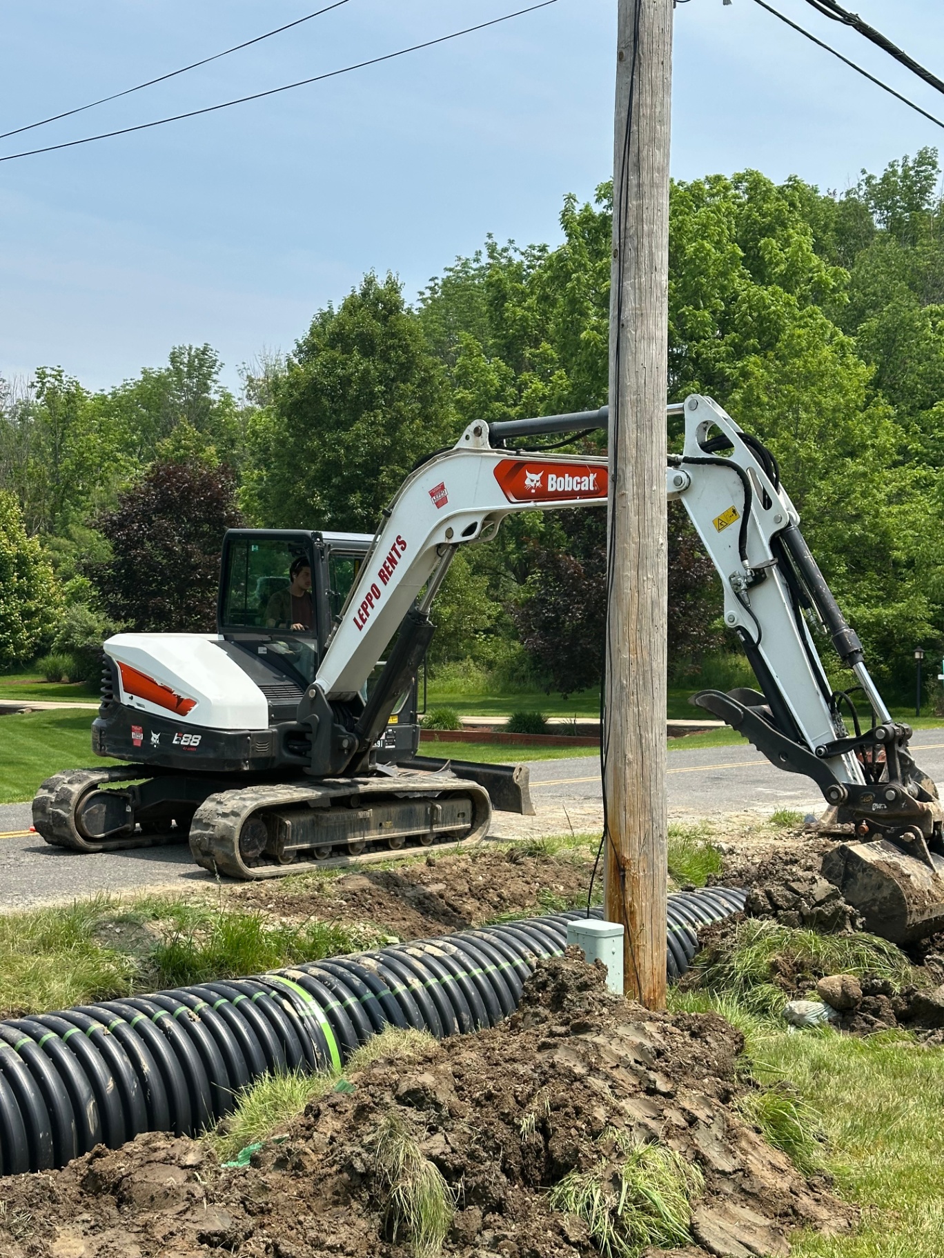 Bobcat excavator installing culvert drainage pipe along a roadside in Medina, Ohio